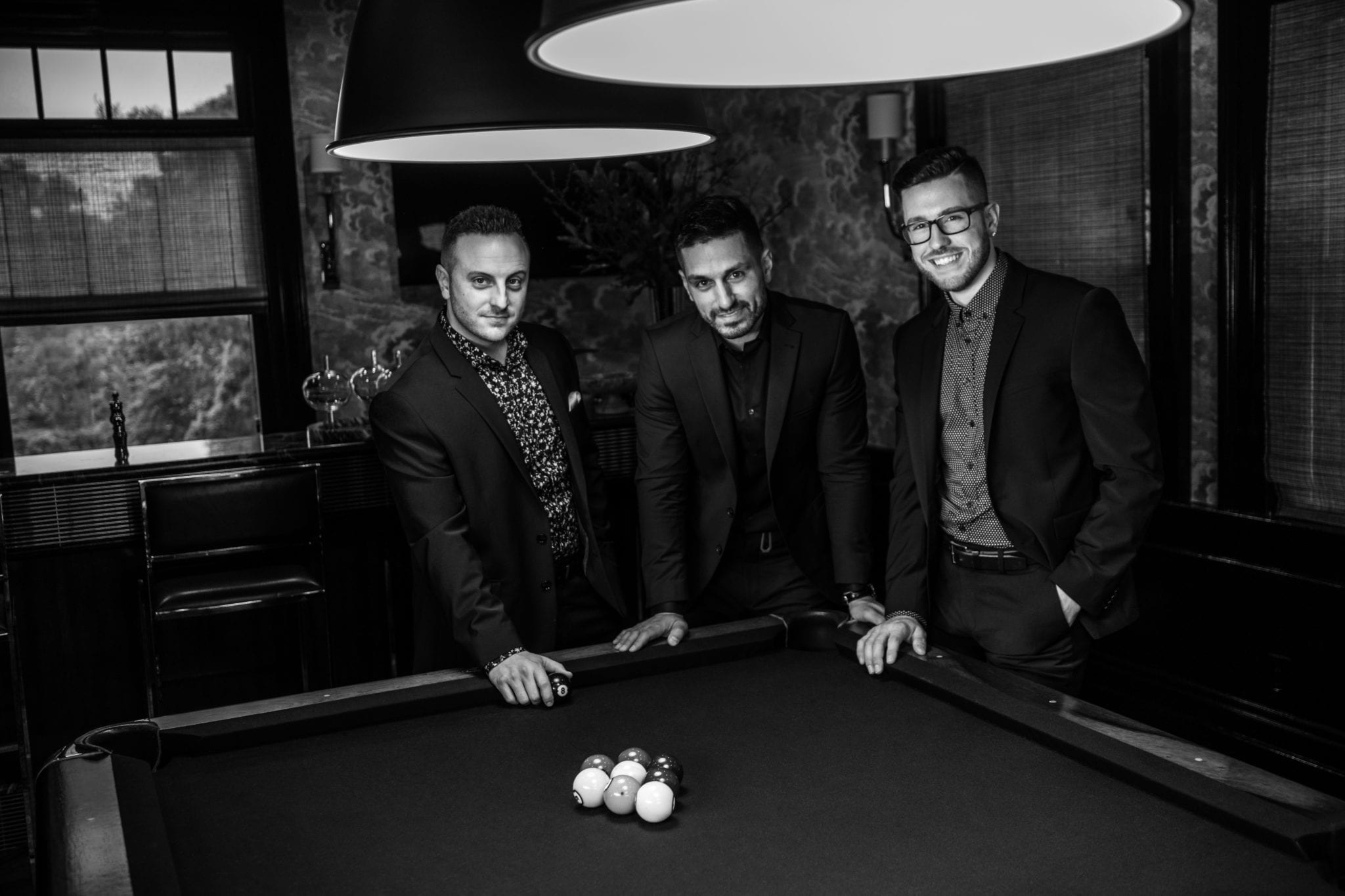 Three men standing by a pool table in suits.