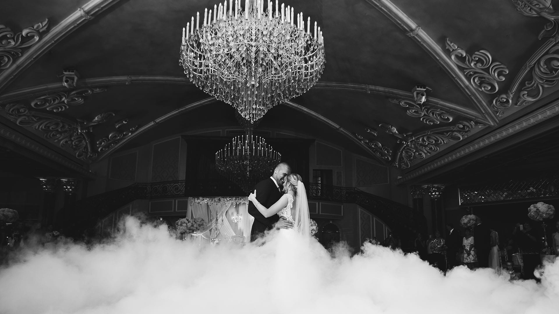 A man and a woman are dancing in a cloud of fog under a chandelier.