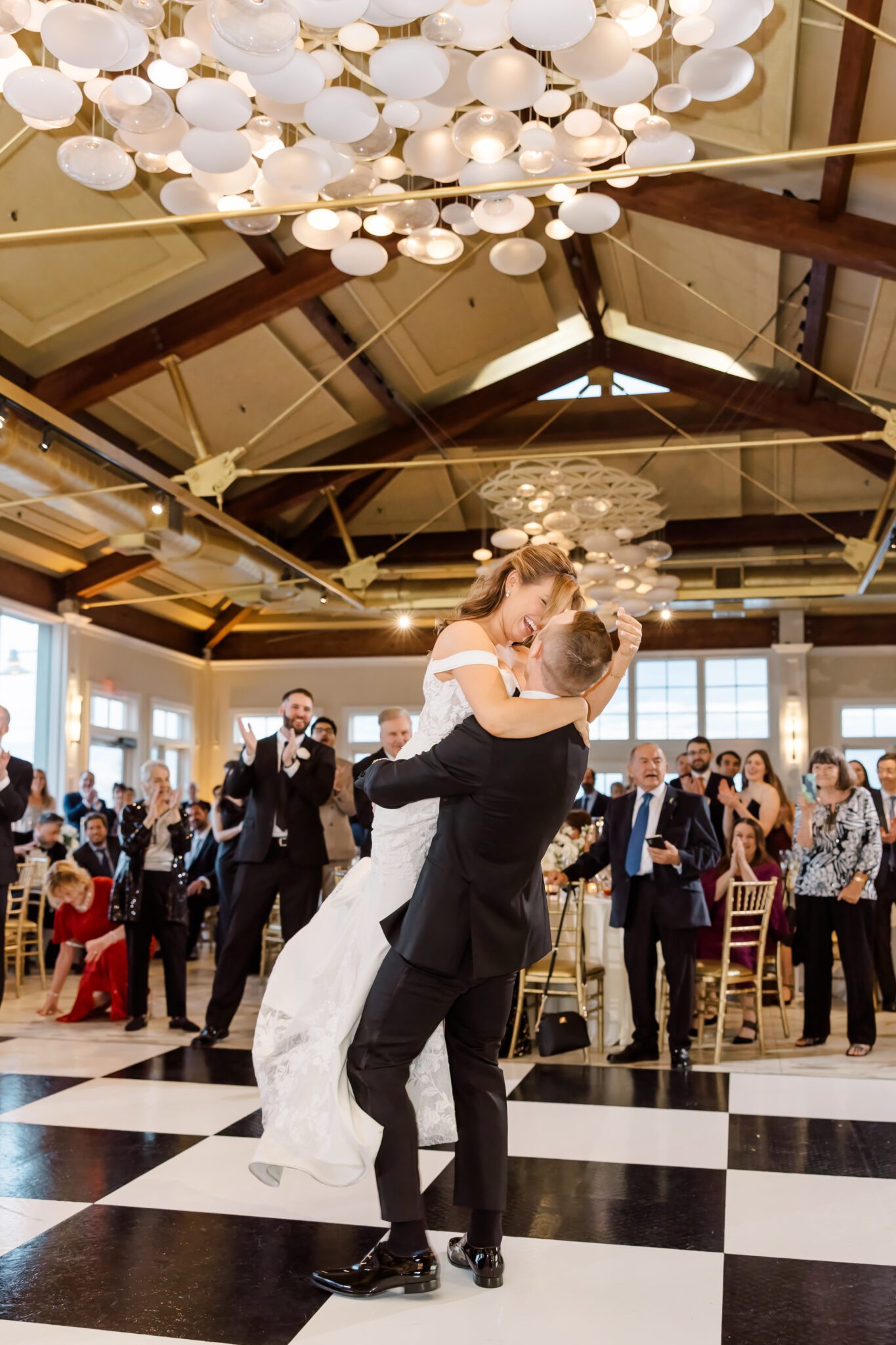 A bride and groom share a joyful moment during their first dance, surrounded by guests who are applauding and celebrating
