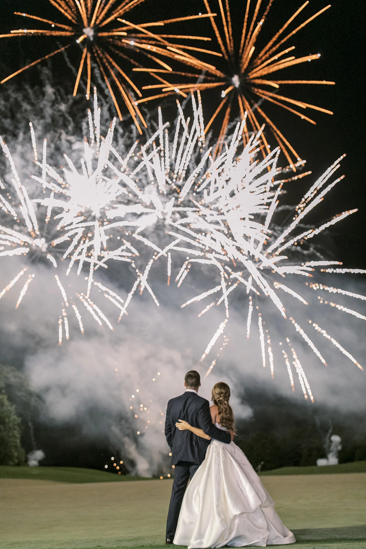 A couple stands together, watching a colorful fireworks display against a night sky