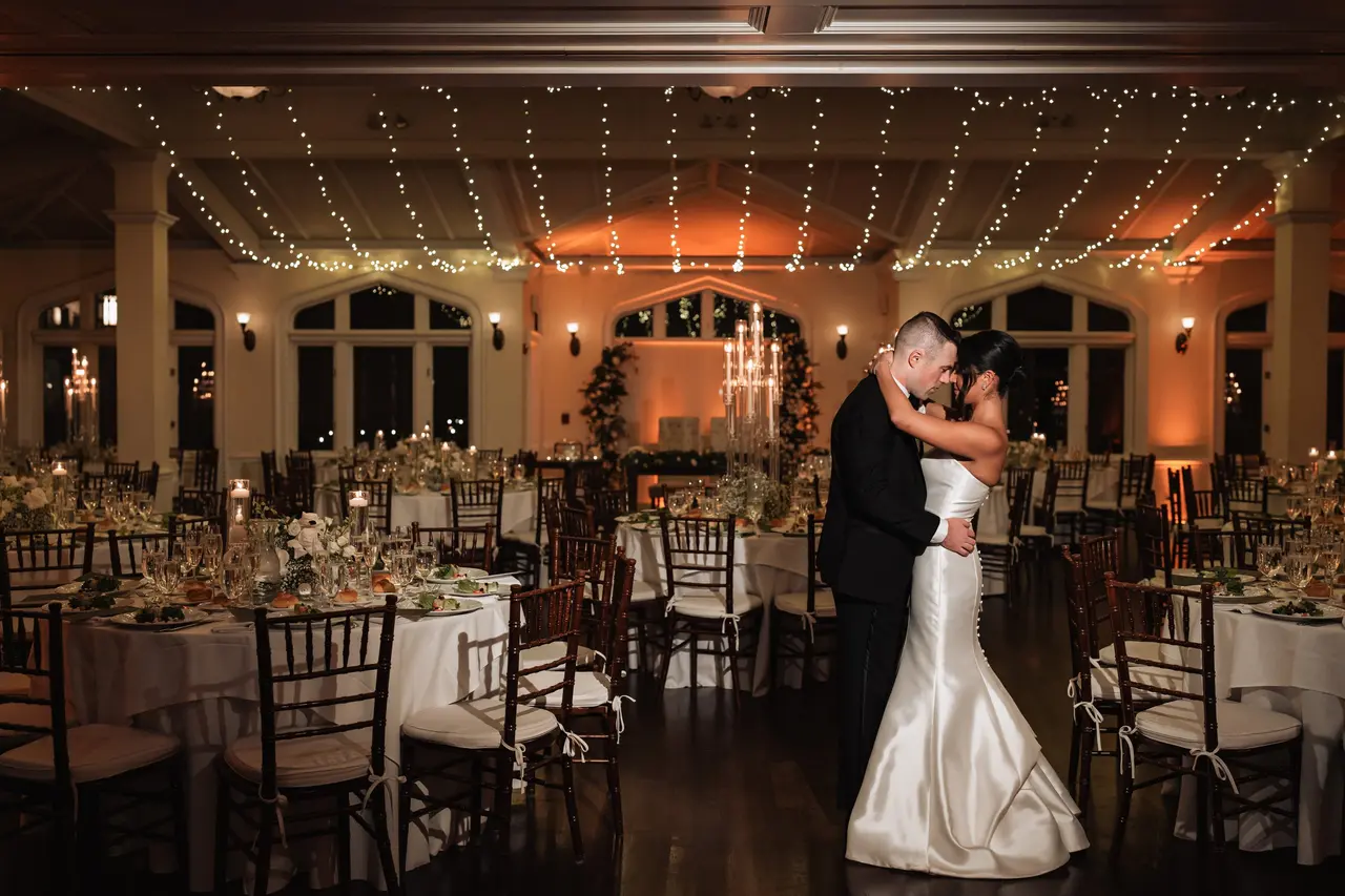 A couple shares a romantic dance in a beautifully decorated reception hall, surrounded by elegantly set tables and soft lighting